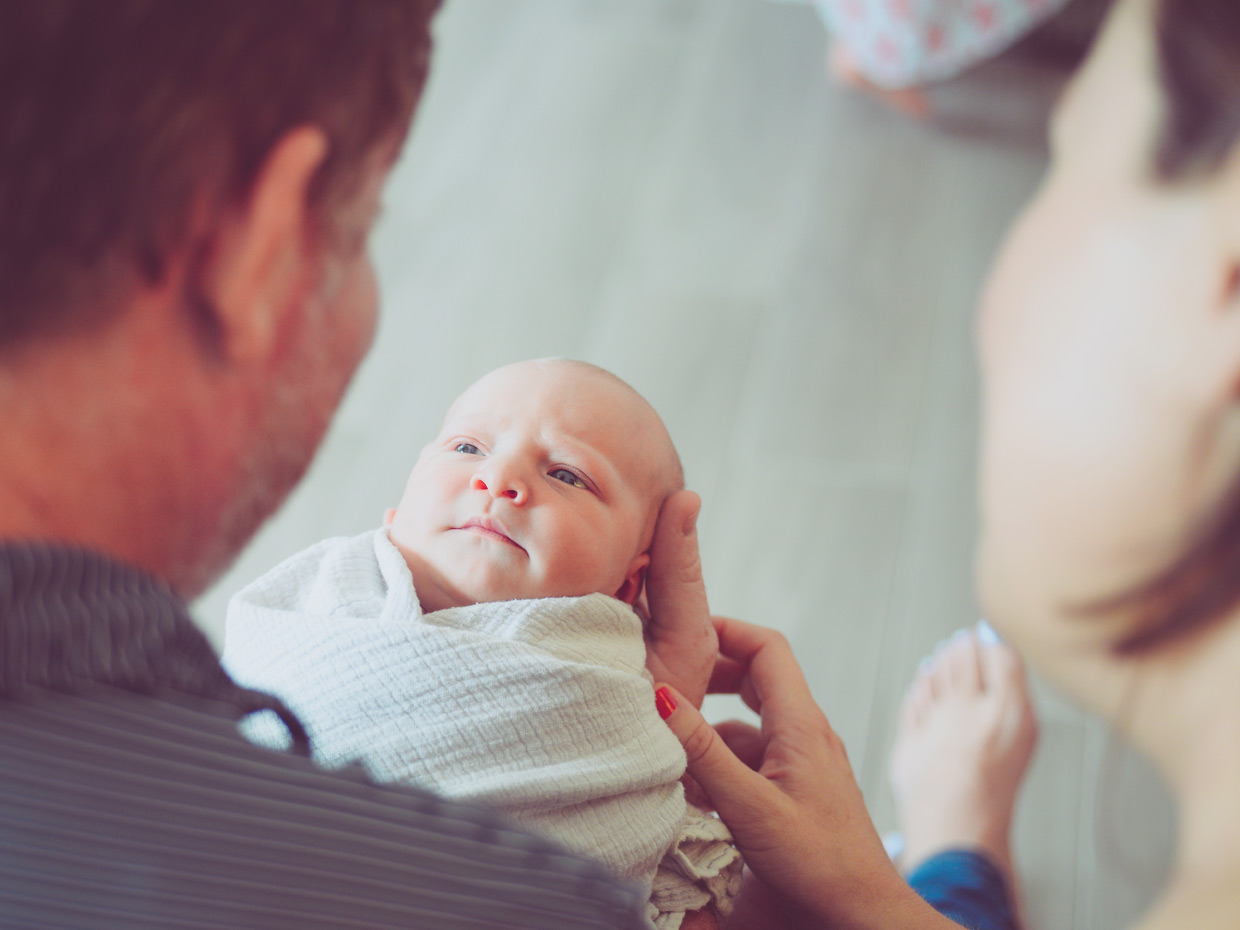 Föräldrar med liten baby i pappans knä ler ner mot barnet.